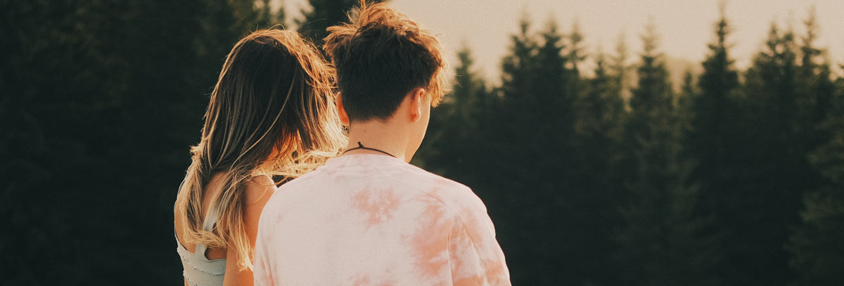 Two people from behind in low sunset light, spruce forest behind them
