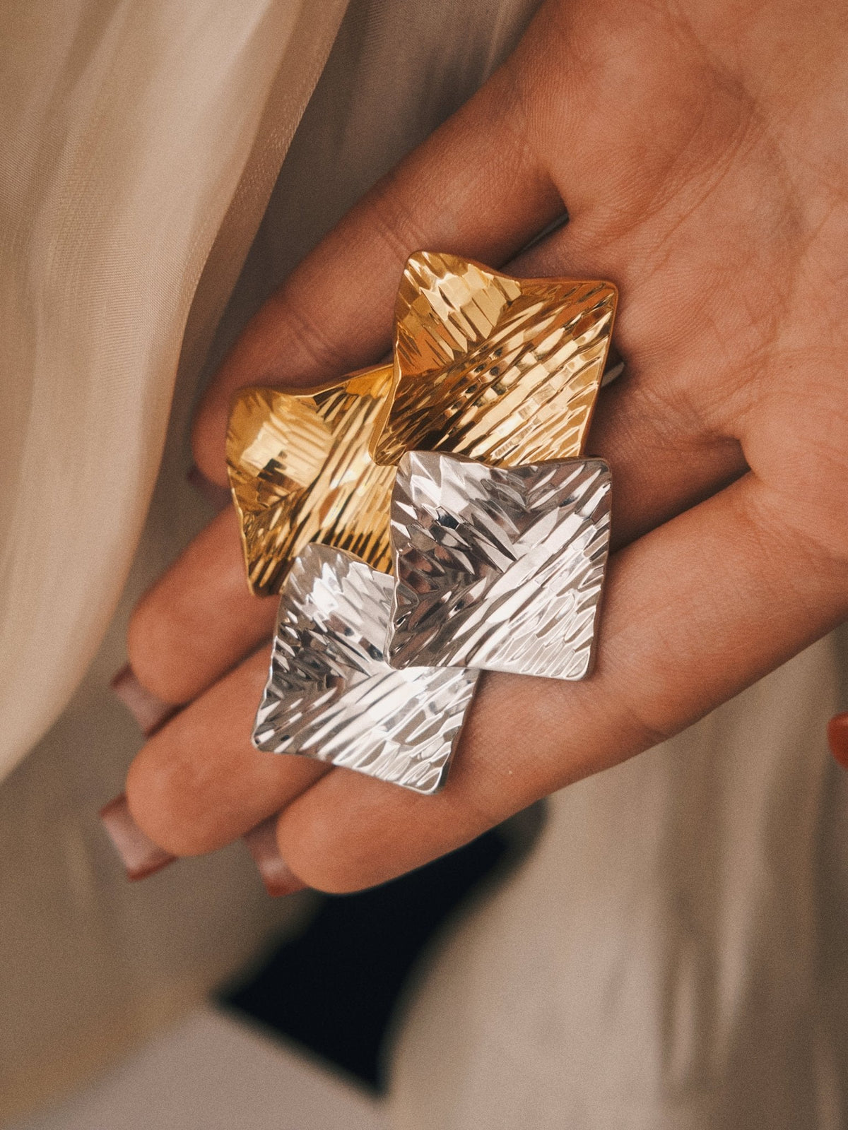 Crushed Metal Square Studs, gold and silver pairs resting on the fingers