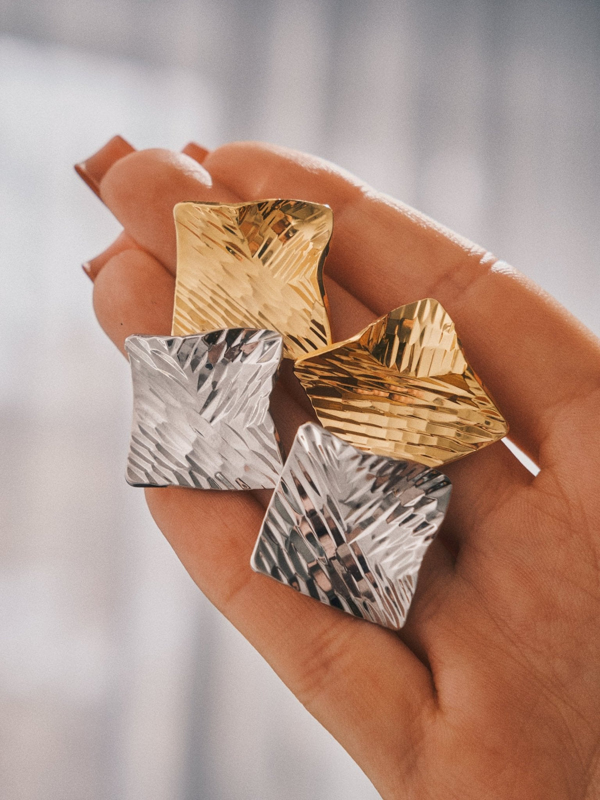 Crushed Metal Square Studs in gold and silver, held in the hand