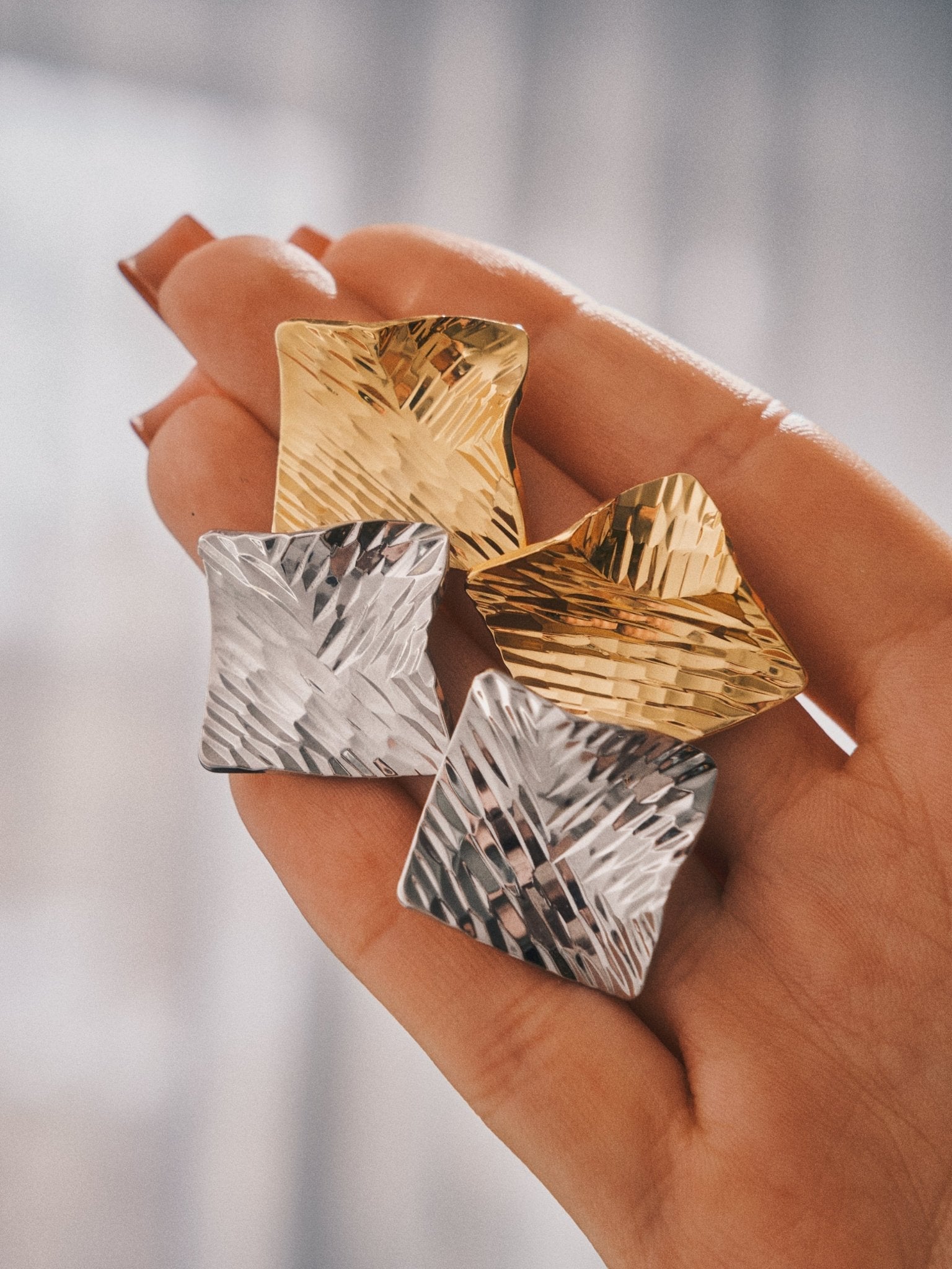 Crushed Metal Square Studs in gold and silver, held in the hand