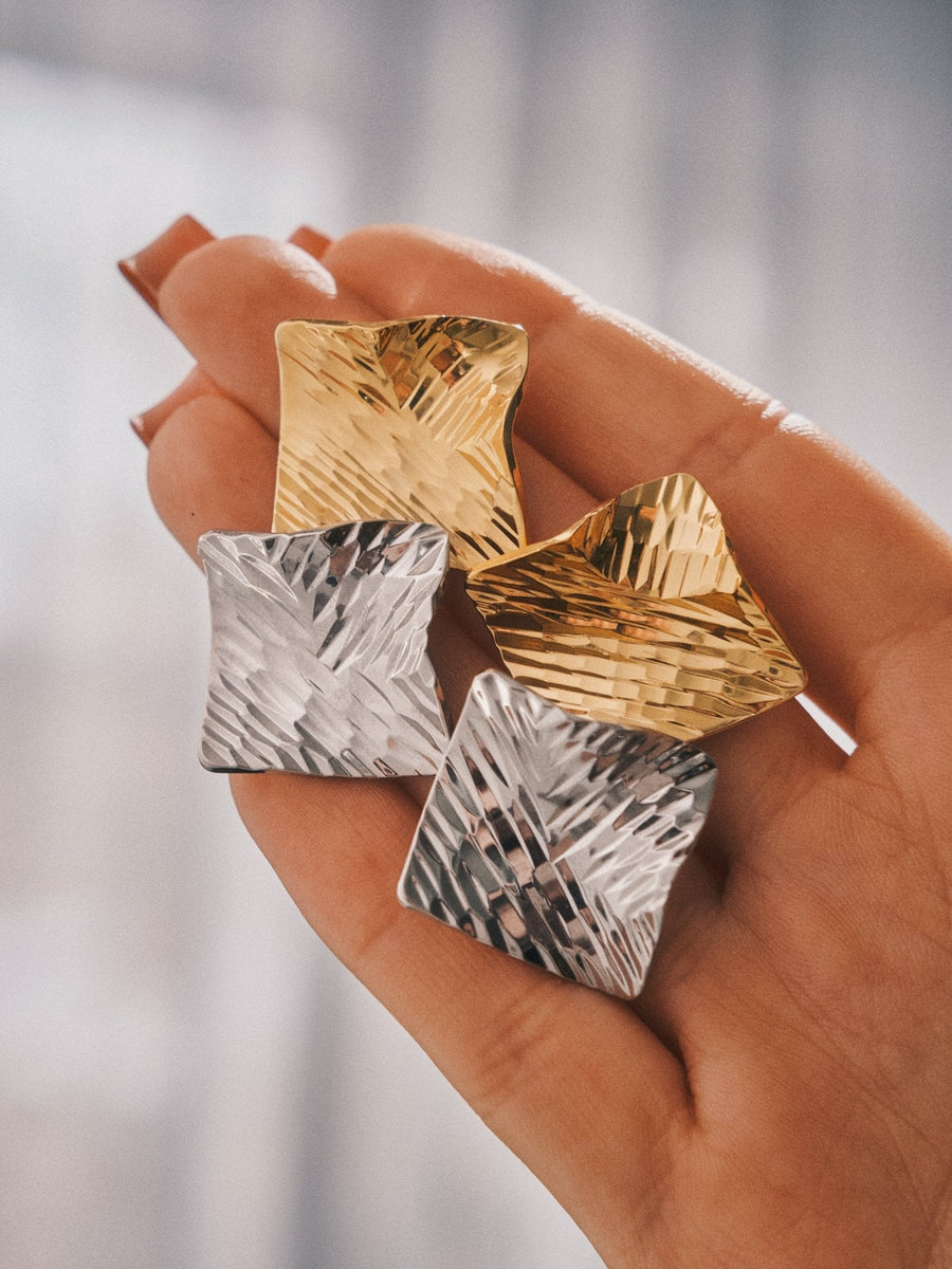 Crushed Metal Square Studs in gold and silver, held in the hand